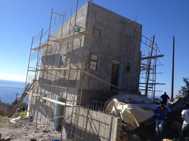 מבנה בבנייה בכרתים עם פיגומים ונוף לים במהלך עבודות הקמה